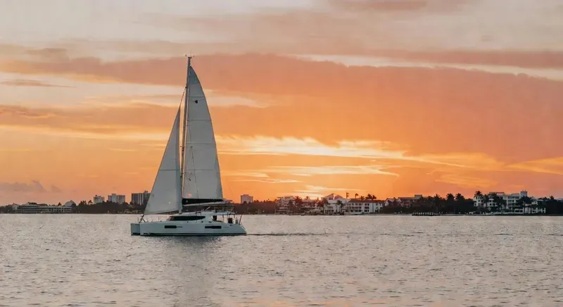 The Spirit of Lauderdale catamaran with full sails at sunset on a Fort Lauderdale champagne sunset cruise, orange sky reflected on the Atlantic Ocean